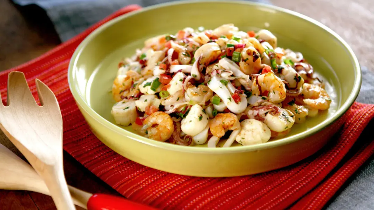 Deliciosa ensalada de marisco con camarones, calamares y vieiras, aderezada con hierbas frescas y pimientos.