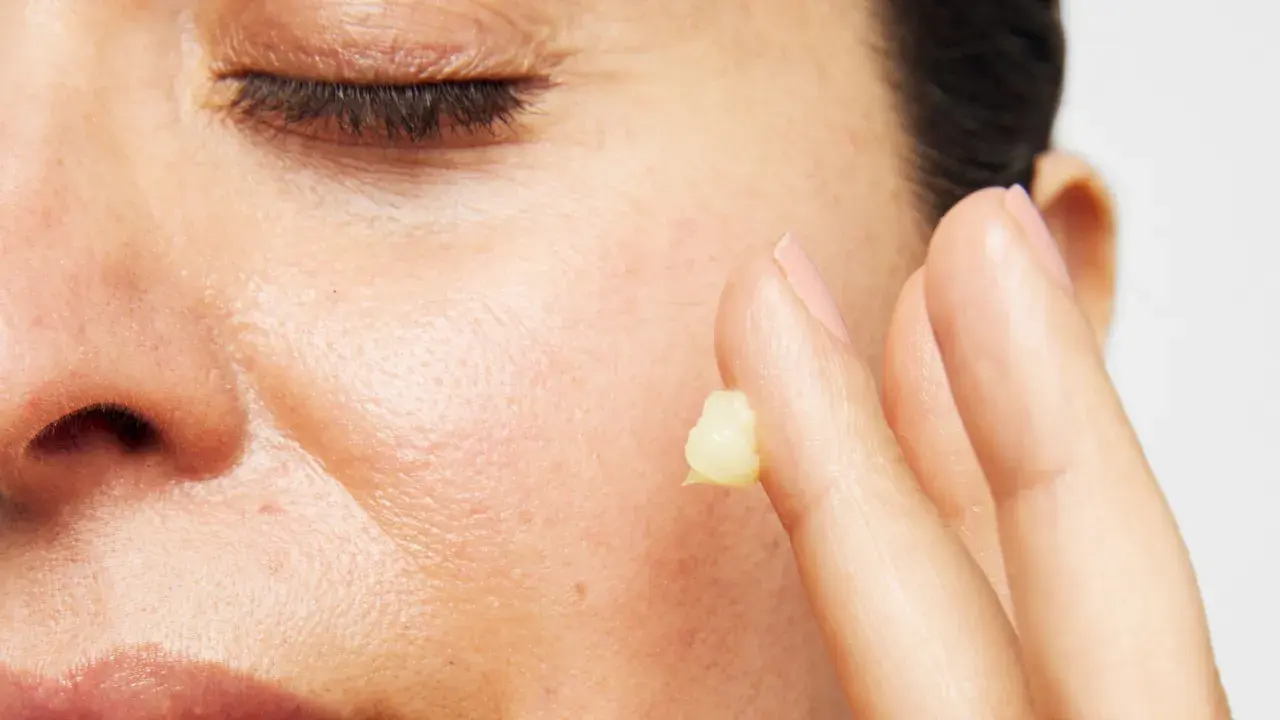 Närbild på en persons ansikte med slutna ögon. Ett finger med en klick kräm, kanske för att visa retinol resultat.