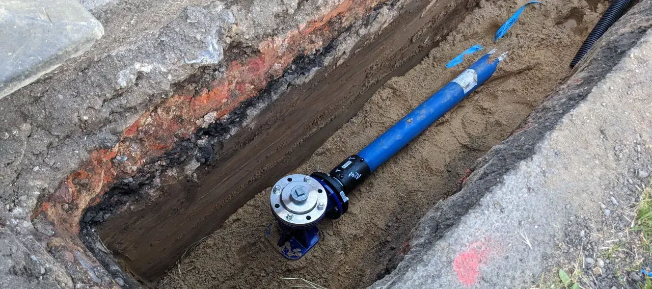 Blaues Rohr mit Ventil in einem ausgehobenen Graben.