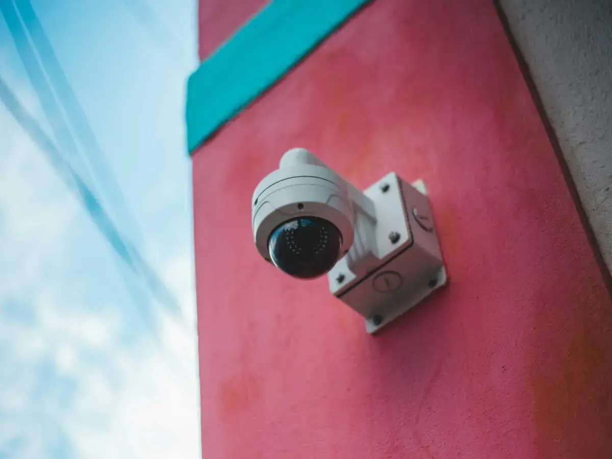 Caméra de surveillance blanche fixée sur un mur rose vif, sous un ciel bleu. Un rappel visuel de la loi sur la caméra de surveillance.