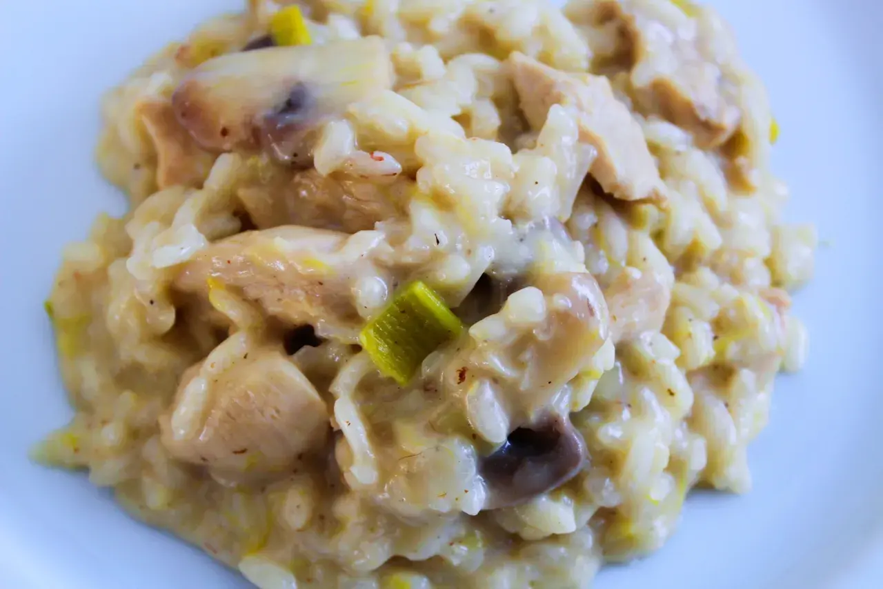 Un crémeux risotto poulet aux champignons et poireaux, servi sur une assiette blanche. Un plat réconfortant et savoureux.