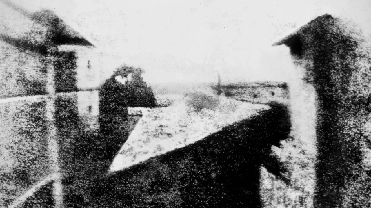 Immagini bianco e nero di un paesaggio urbano con edifici e cielo. La prospettiva è dall'alto, con un tetto in primo piano.