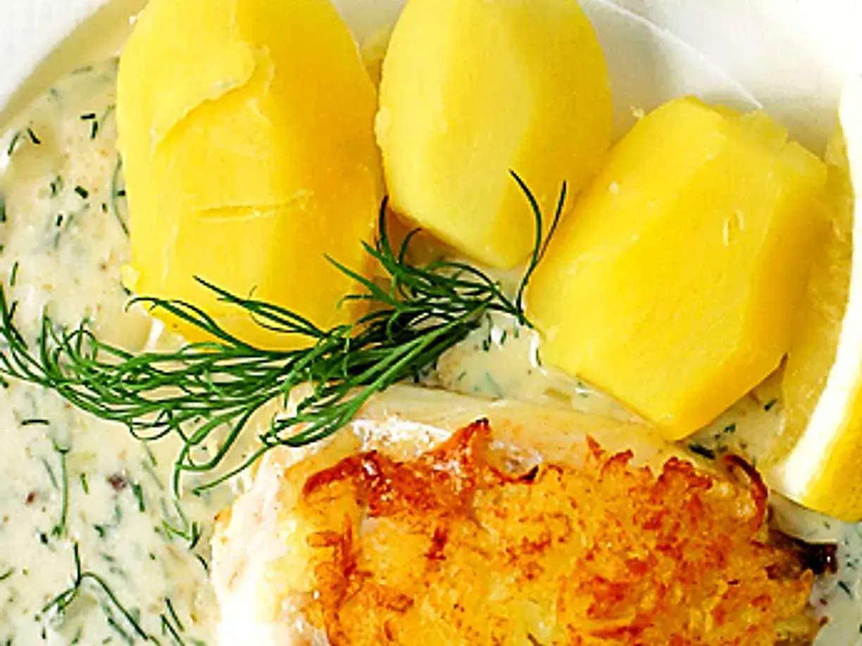 En gyllene fiskbit med krämig dillsås till fisk, serverad med kokt potatis och en citronskiva.