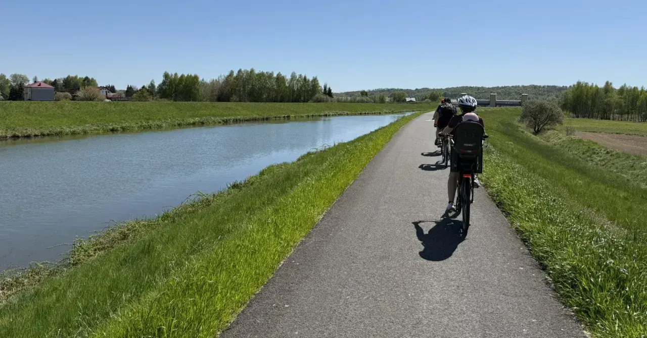 Rodzina na rowerach wzdłuż kanału. Słoneczny dzień sprzyja rodzinnemu **velo skawa** pośród zielonych łąk i drzew.