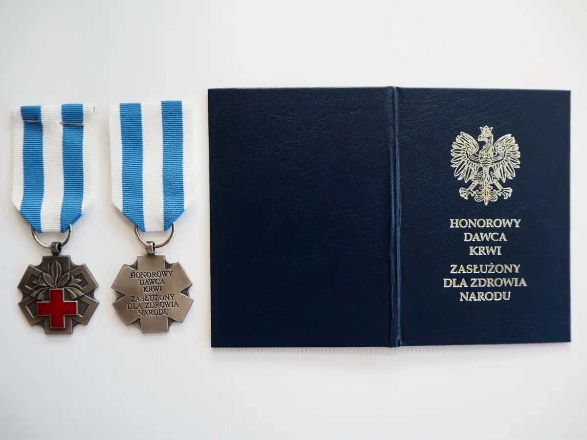 Dwa medale z czerwonym krzyżem i napisem "Honorowy Dawca Krwi Zasłużony dla Zdrowia Narodu" oraz granatowa teczka z godłem Polski.