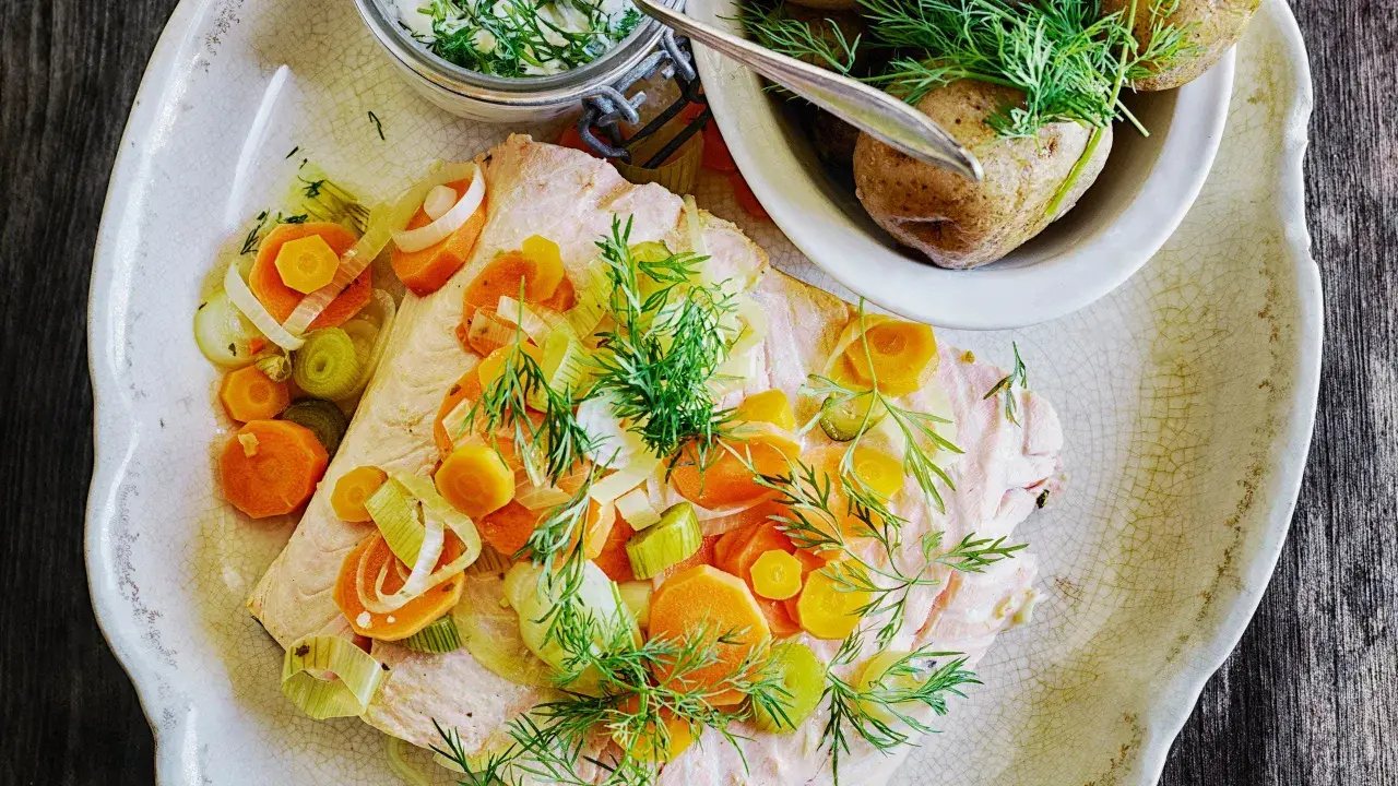 En vacker portion inkokt lax med morötter, purjolök och dill. Serveras med kokt potatis och en krämig sås.
