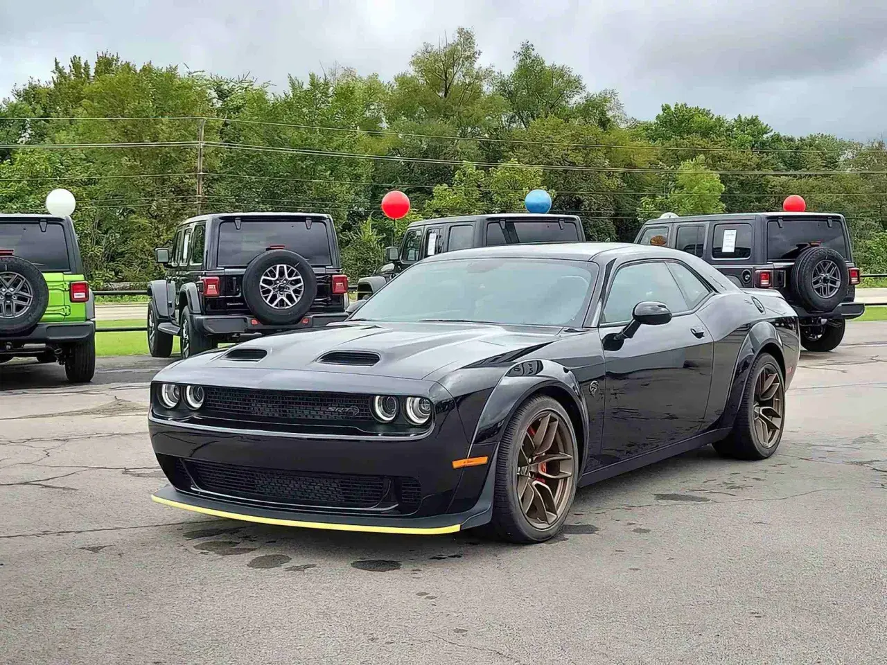 Czarny Dodge Challenger SRT z żółtym akcentem na zderzaku. Obok inne samochody i balony. Sprawdź dodge challenger cena!