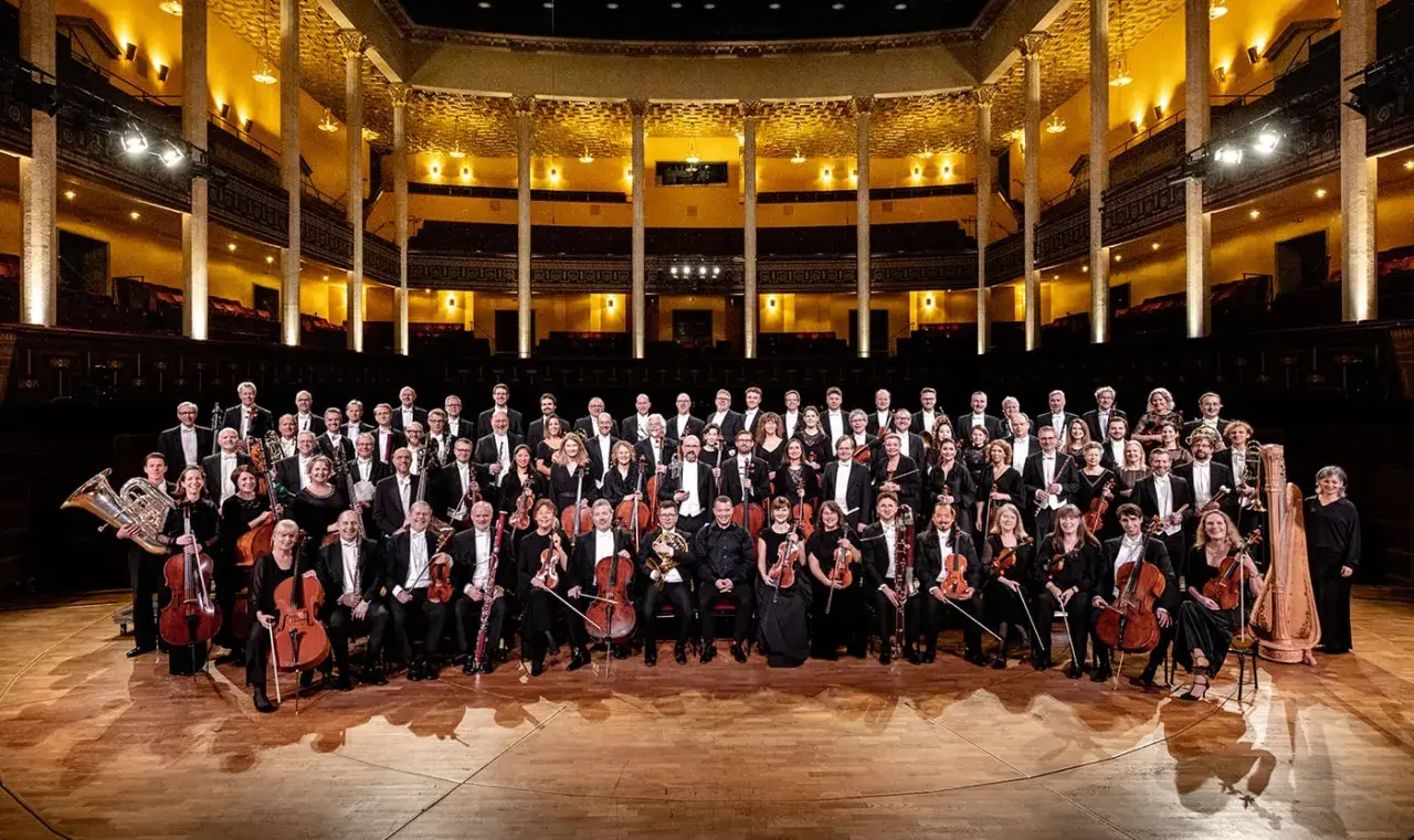 Kungliga Filharmonikerna medlemmar poserar i en stor orkestersal.
