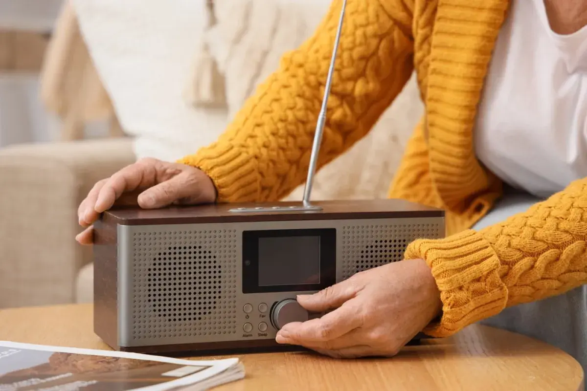 Dłoń kręci pokrętłem radia, by posłuchać RMF FM w pracy.