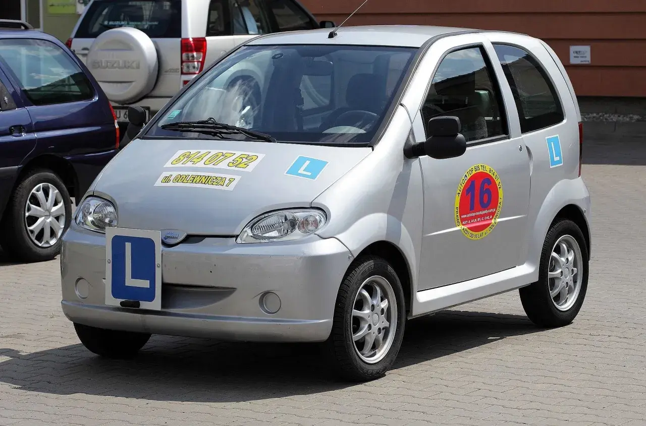 Srebrny czterokołowiec z literą "L" na masce i z boku, gotowy do nauki jazdy.
