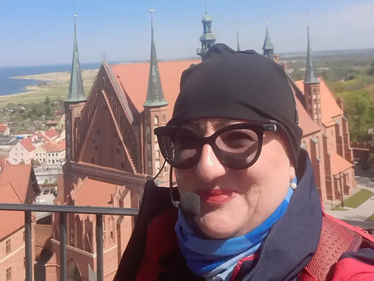 Kobieta w okularach i czapce na tle Fromborka. Wspaniałe widoki, idealne na rodzinne wycieczki i atrakcje dla dzieci.