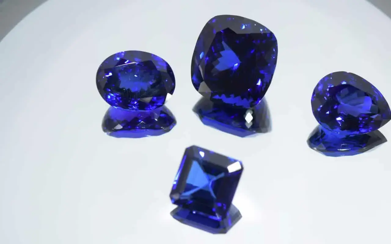 Cinco gemas de tanzanita piedra, de cortes y tamaños variados, brillan con un intenso color azul sobre un fondo reflectante.