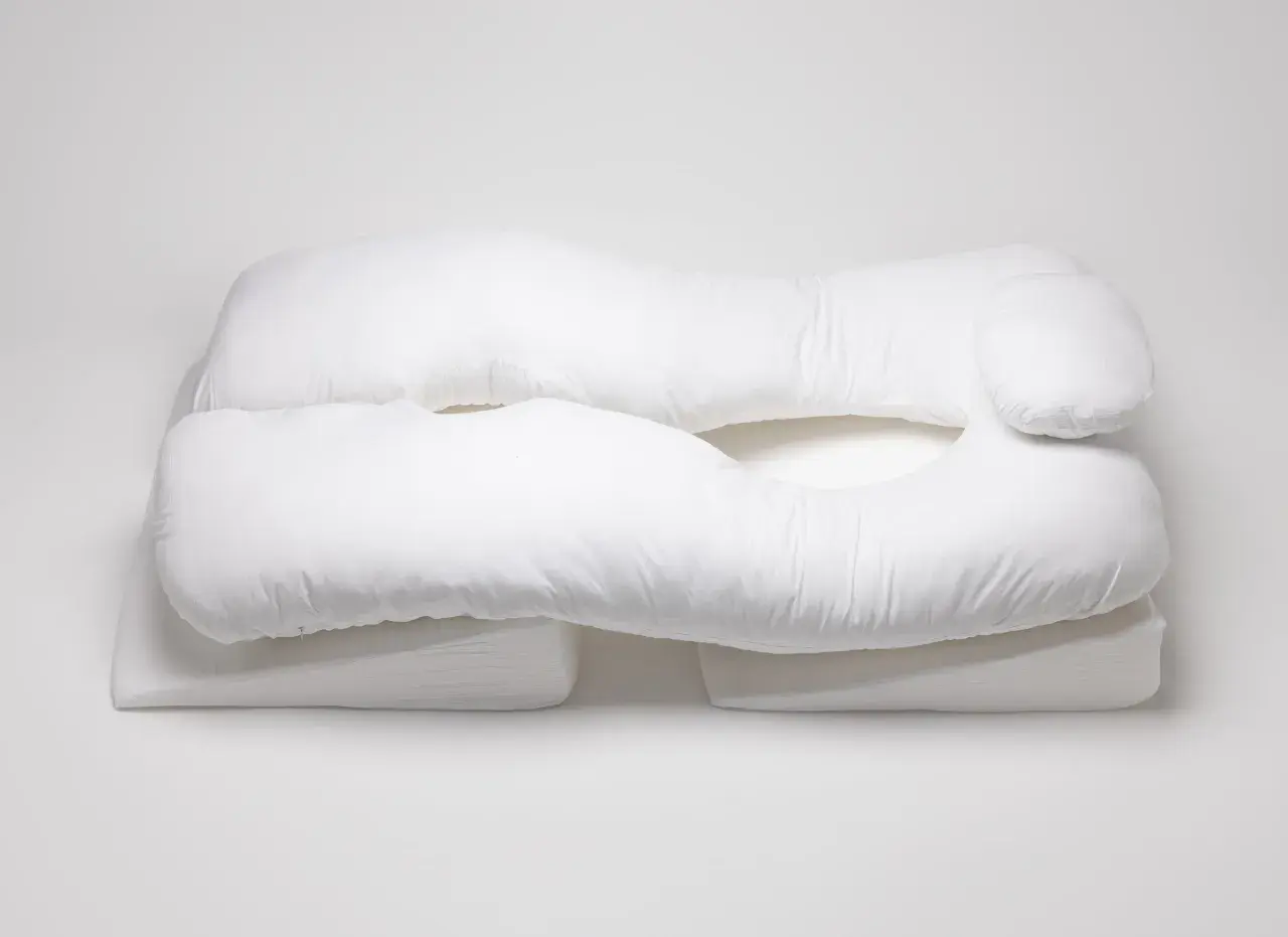 A white, U-shaped body pillow, designed for comfort and support, rests on wedge-shaped cushions. These almohadas ortopédicas offer a cozy embrace.