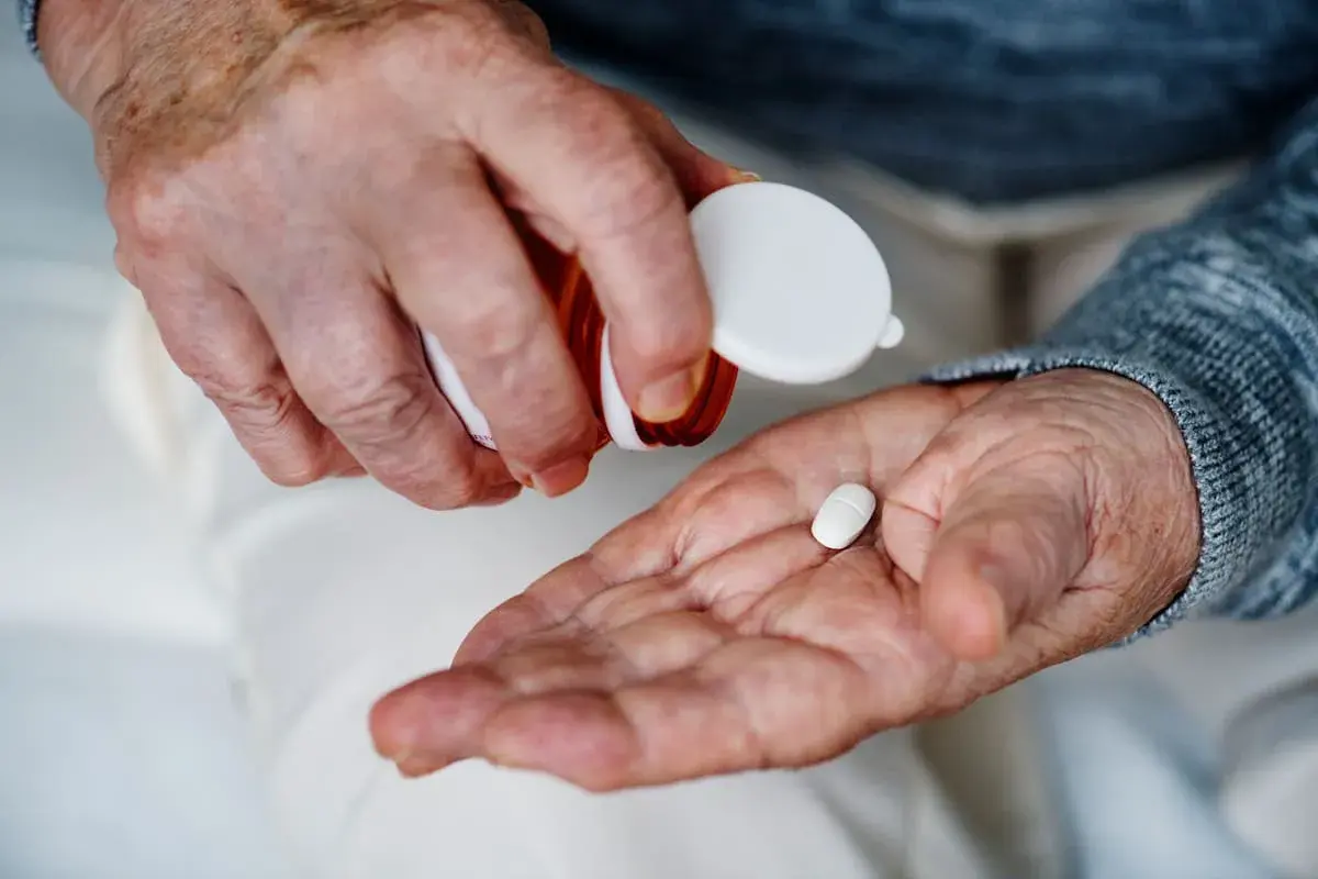 Manos de anciano vertiendo una pastilla blanca en su palma para tomar magnesio.