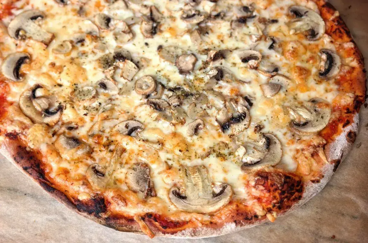 Pyszna pizza capricciosa z pieczarkami i ciągnącym się serem, idealna na wieczór z przyjaciółmi.