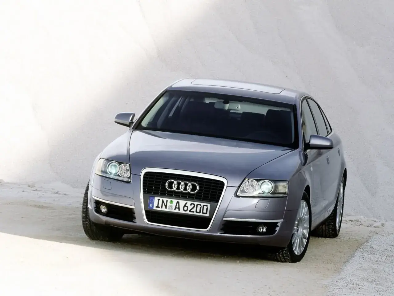 Szary Audi C6 z tablicą rejestracyjną IN A 6200 stoi na piaszczystym podłożu.