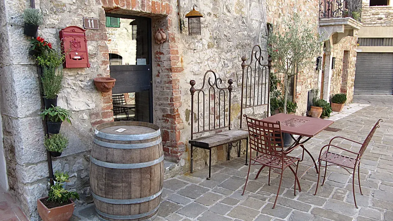 Un angolo pittoresco nella regione del Chianti con un barile di legno, piante aromatiche, un tavolino da esterno e un vecchio cancello in ferro battuto.