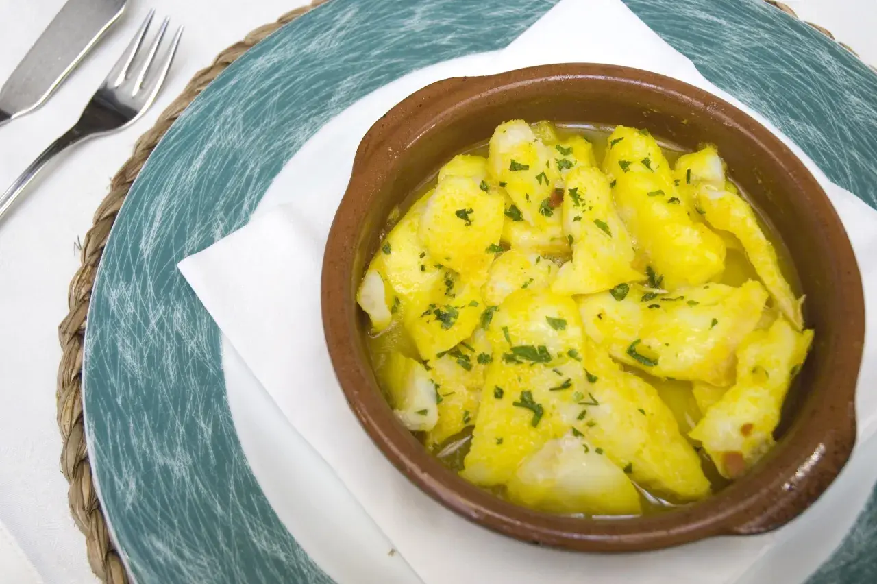 Delicioso bacalao a la cazuela, con trozos tiernos de pescado en una salsa dorada y perejil picado, servido en una cazuela de barro.