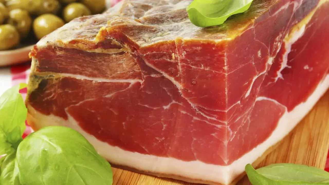 Ein Block Parma-Schinken, mariniert mit Kräutern, daneben grüne Oliven. Was ist Parmaschinken? Ein Genuss!
