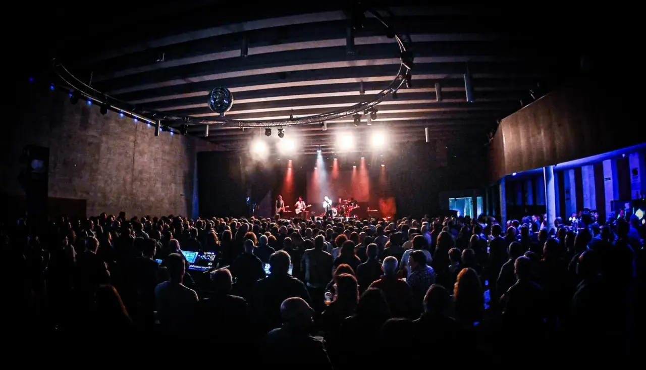 Un concierto en un **escenario Santander** lleno de gente, con luces rojas y blancas iluminando a la banda.