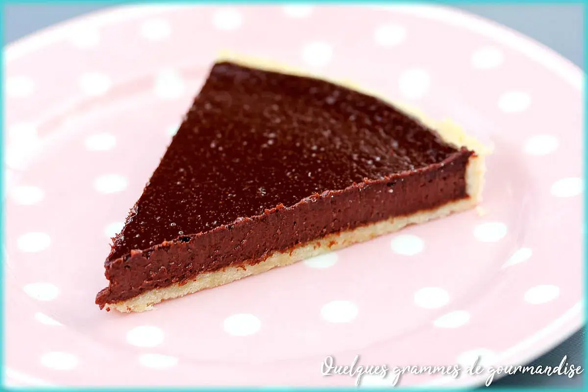 Une part de tarte au chocolat facile, avec une garniture riche et une pâte croustillante, servie sur une assiette rose à pois blancs.