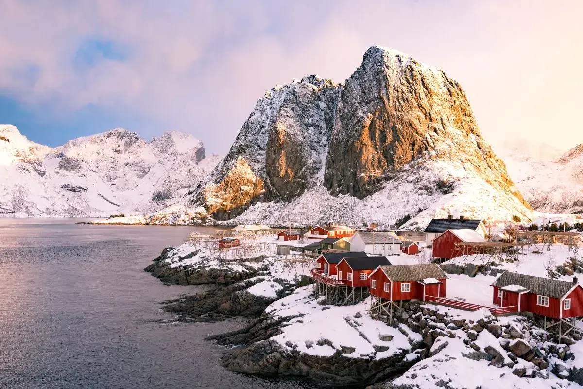Village de pêcheurs aux maisons rouges sur pilotis, sous des montagnes enneigées. Un paysage typique de la Norvège.