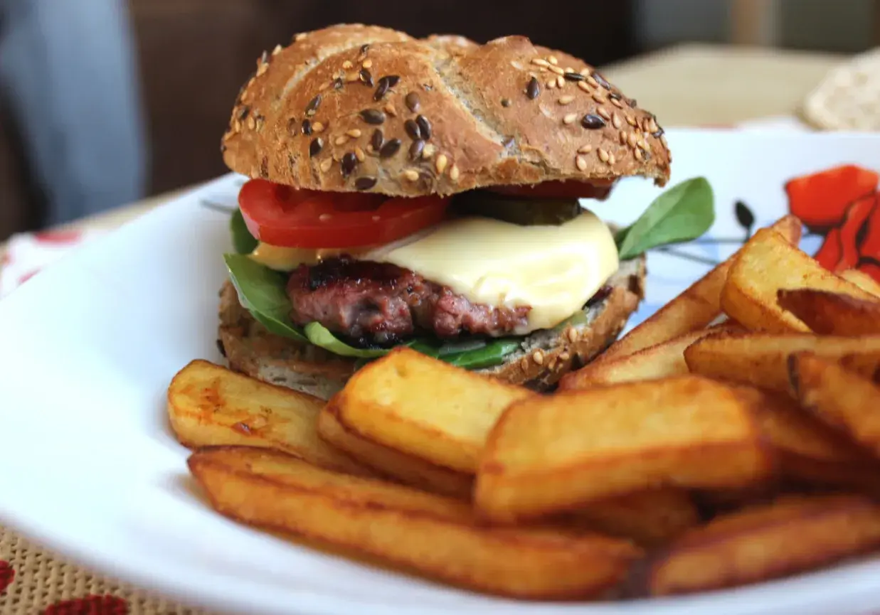 Soczysty burger wołowy z serem, pomidorem i frytkami na talerzu.