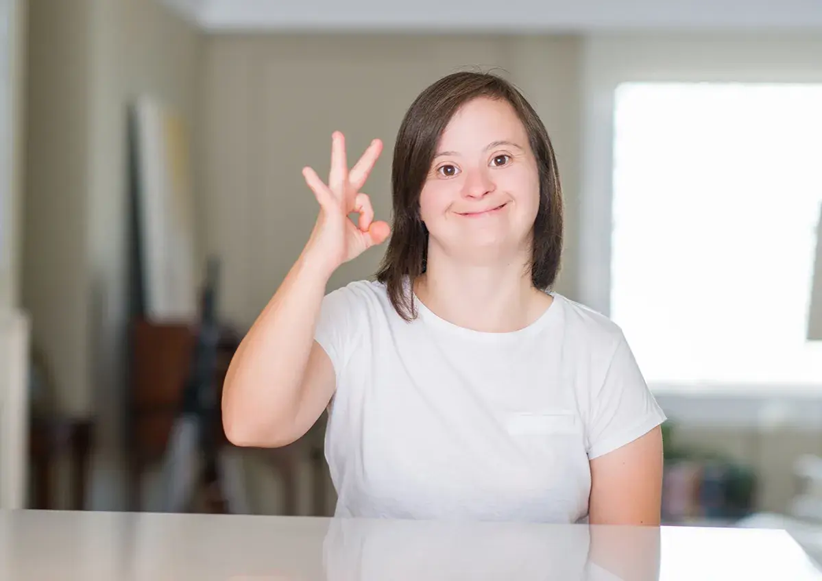 Ragazza con sindrome di down sorride e fa il segno "ok" con la mano.