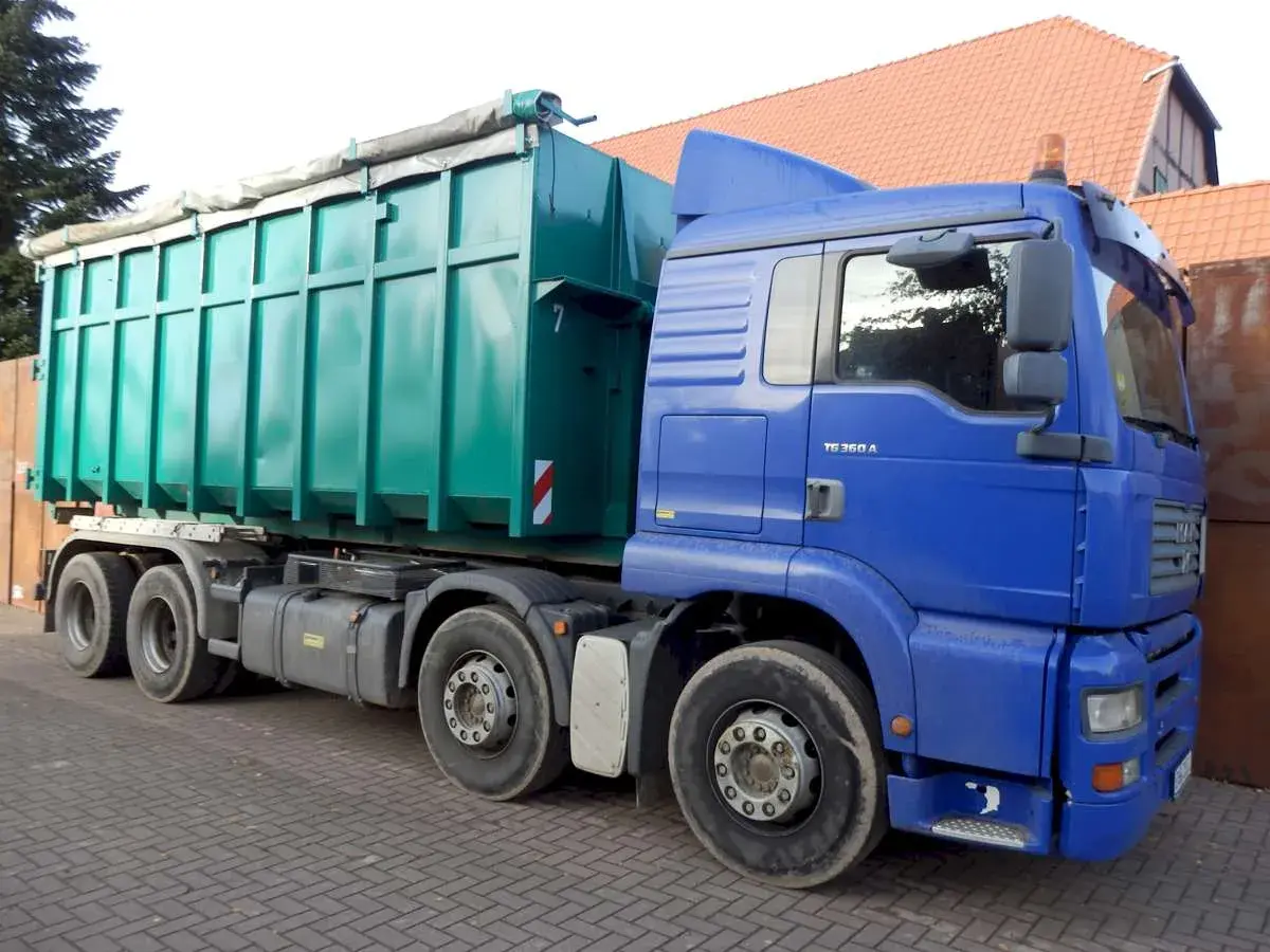 Blauer LKW mit großem grünen Container. Die Bedeutung eines solchen LKW ist der Transport von Schüttgut oder Abfall.