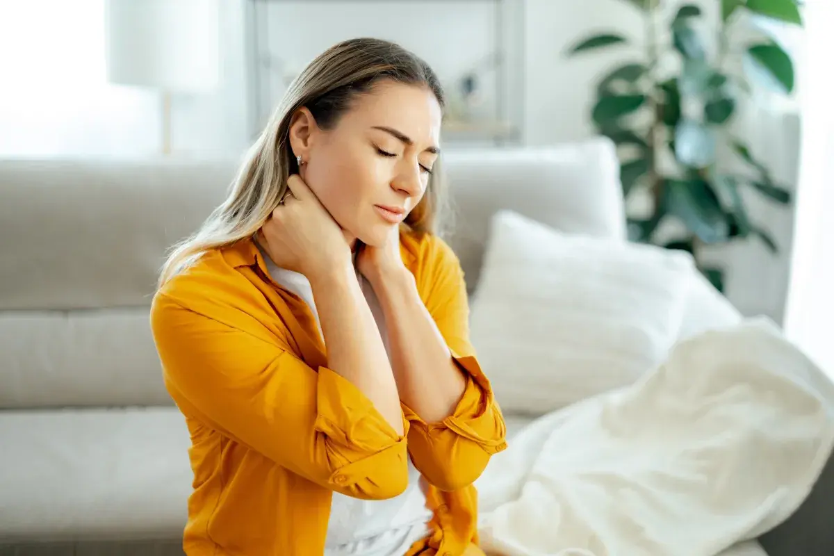 Donna con occhi chiusi e mani sul collo, soffre di dolori muscolari diffusi.