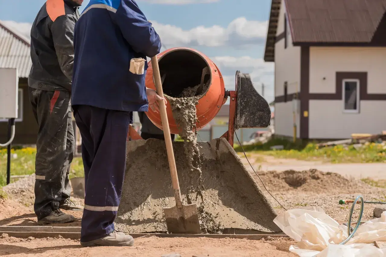 Dwóch budowlańców pracuje przy betoniarce. Wylewa się z niej świeży beton. Pytanie: ile cementu na betoniarkę 200?