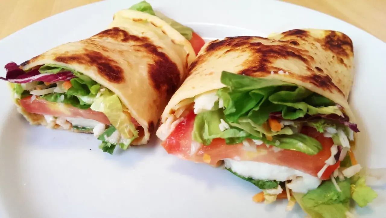 Zwei herzhafte Pfannkuchen gefüllt mit Salat, Tomaten und Käse auf einem weißen Teller.