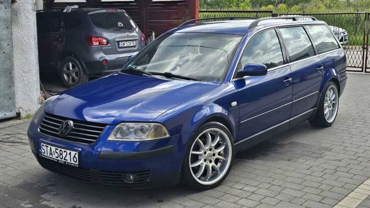 Błękitny Passat B5 1.9 TDI 130KM na aluminiowych felgach, zaparkowany na podjeździe obok szarego SUV-a.
