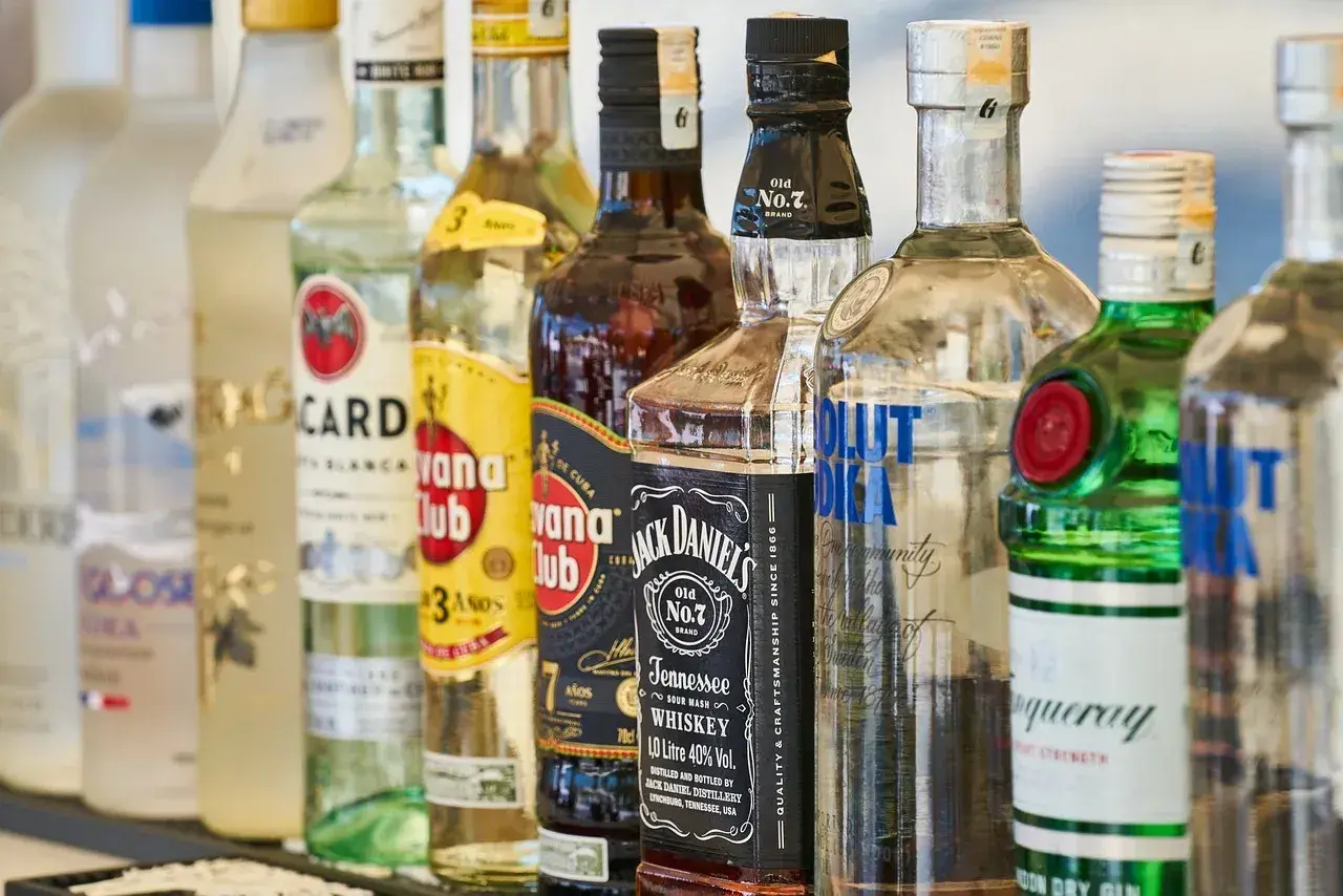 Rząd butelek alkoholi, w tym wódki, whisky i ginu, na barze.