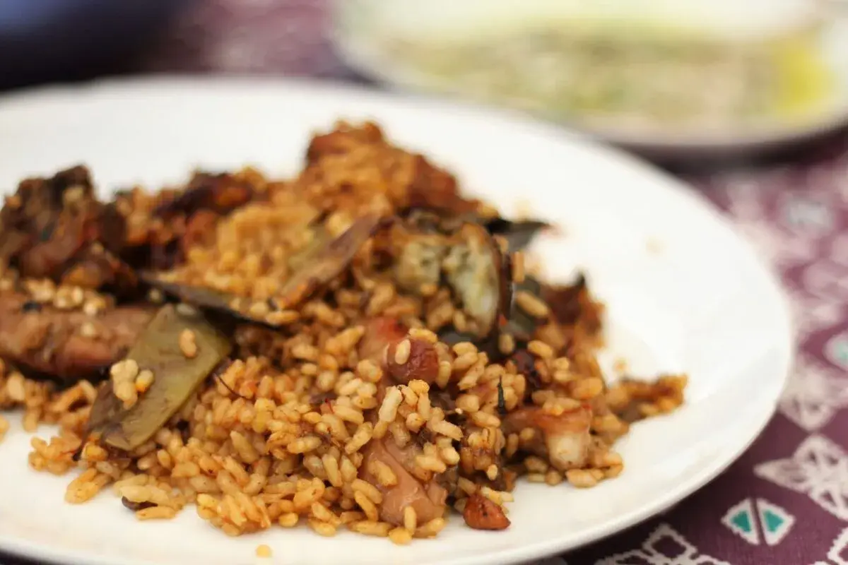 Deliciosa paella de conejo con trozos de carne dorada y verduras, servida en un plato blanco.