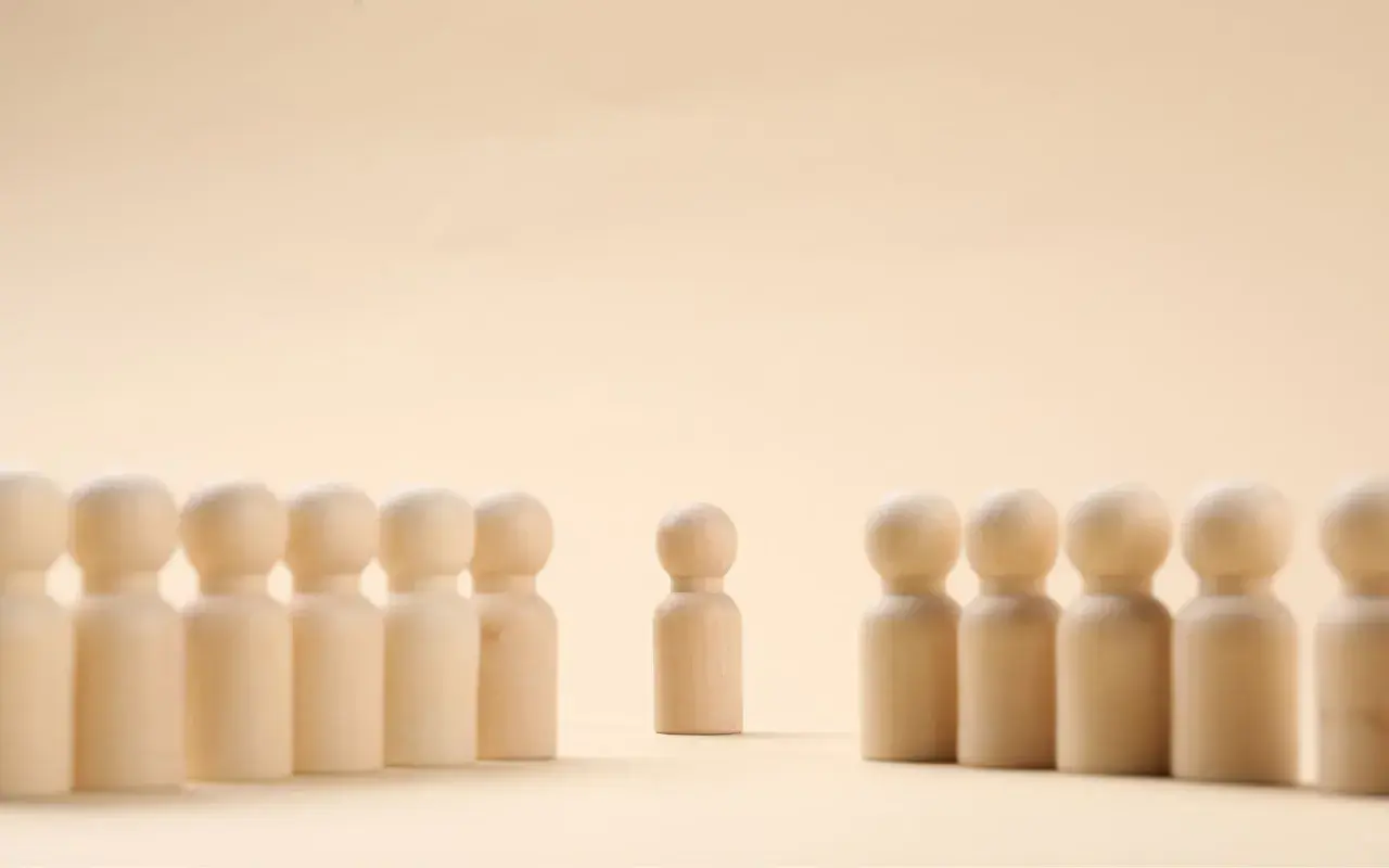 Un pupazzetto di legno si erge da solo, separato da un gruppo. Un simbolo di imparare a stare da soli, trovando forza nella propria individualità.