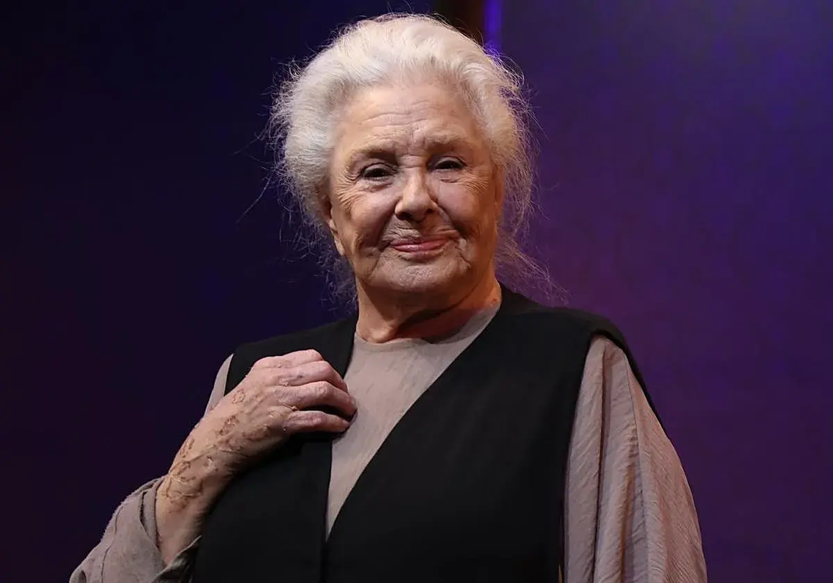 Lola Herrera, con su melena plateada y una sonrisa serena, luce un chaleco negro sobre una blusa beige. Su mano izquierda, con un anillo, reposa sobre su pecho.