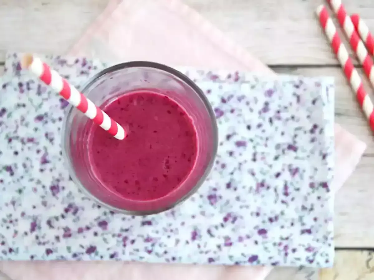 En glas med en lila indisk yoghurtdryck, med ett rött och vitt randigt sugrör.