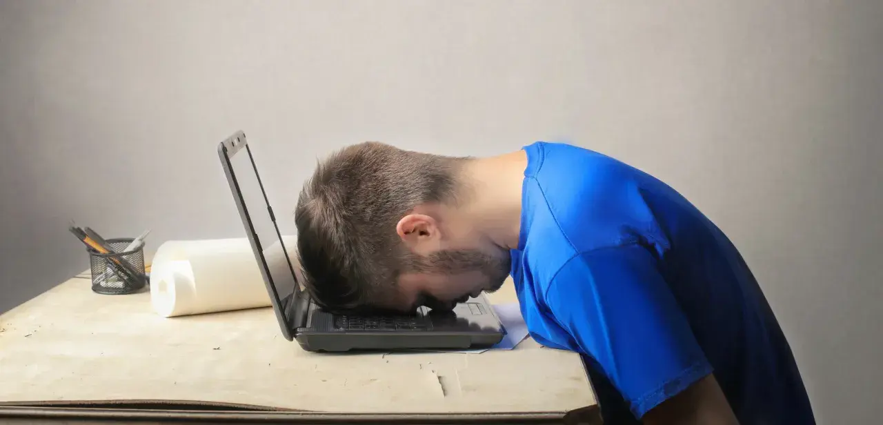 Frustrierter Mann mit Kopf auf Laptop. Er sucht nach einem Musterbrief für den Widerruf einer Abo-Falle.