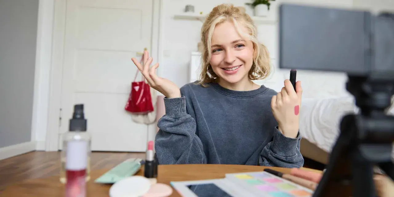 Uśmiechnięta influencerka z pomadką na dłoni pokazuje, jak zostać ambasadorem marki, nagrywając tutorial makijażowy.