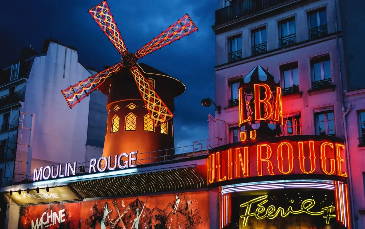 Le Moulin Rouge à Paris s'illumine la nuit, ses ailes de moulin rouge et jaune dansant sous le ciel sombre.