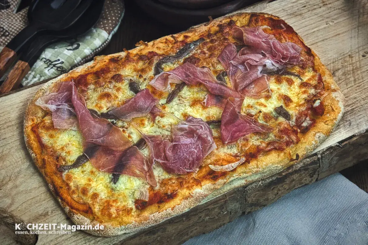 Frisch gebackene Pinsa mit zartem Schinken und geschmolzenem Käse auf rustikalem Holzbrett. Ein Genuss für jeden, der gerne Pinsa backen möchte.