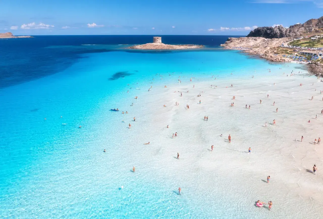 Türkises Wasser und ein alter Turm auf Sardinien. Menschen genießen das flache, klare Meer an einem sonnigen Tag.