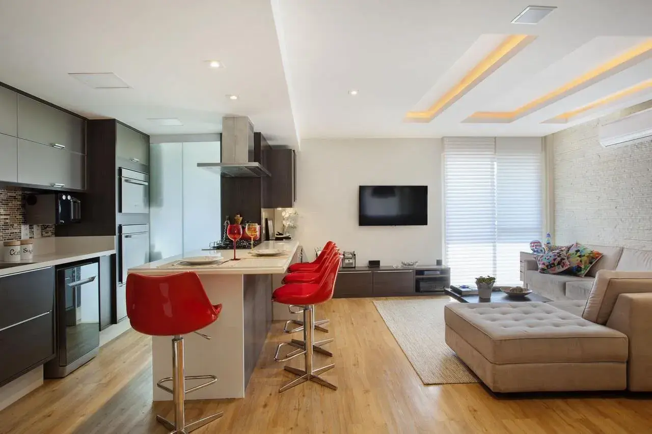 Cucina moderna con isola e sgabelli rossi, soggiorno con divano e TV. Il soffitto in cartongesso design crea un'atmosfera accogliente.