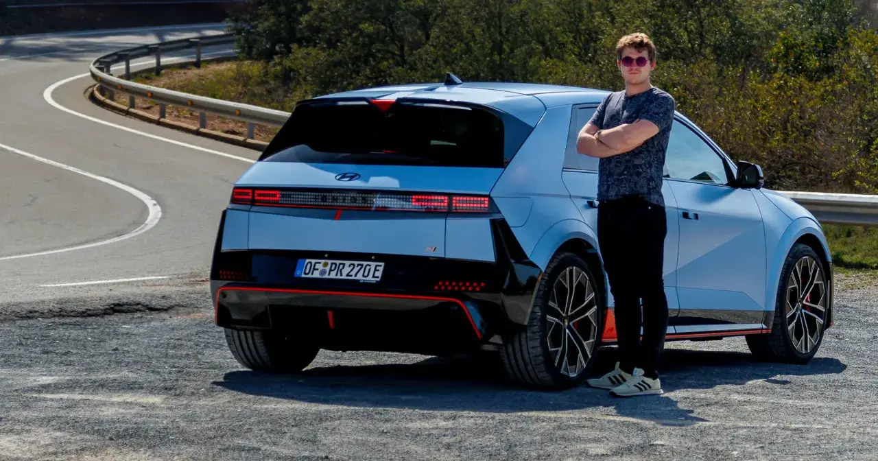 Młody mężczyzna w okularach stoi obok sportowego Hyundai Ioniq 5 N na krętej drodze.