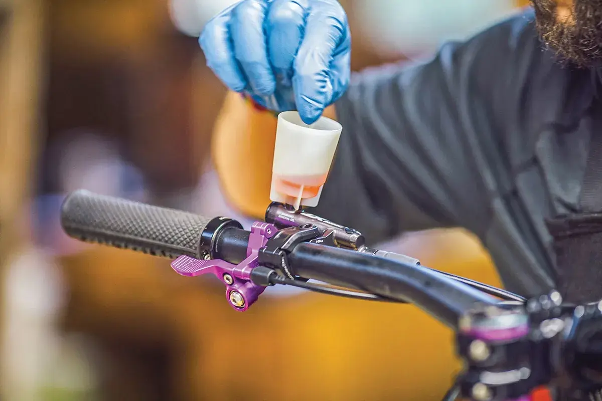 Gloved hand pours fluid into a bike's brake lever, a step in learning how to bleed hydraulic lines.