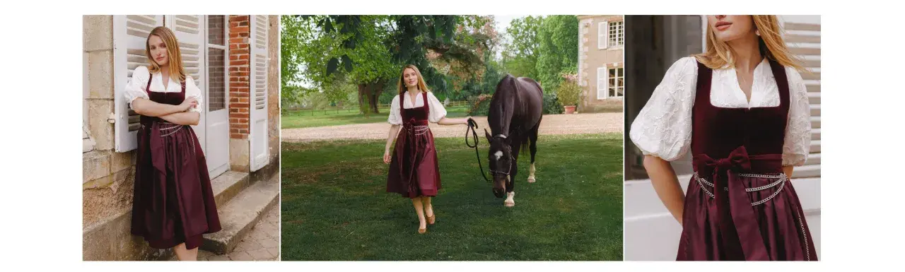 Eine Frau in einem weinroten Dirndl mit einer glänzenden Dirndlschürze aus Seide, daneben ein Pferd auf einer grünen Wiese.