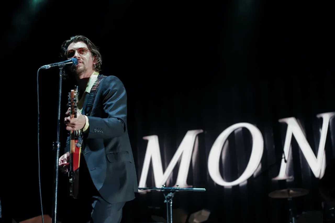 Alex Turner w okularach przeciwsłonecznych śpiewa i gra na gitarze podczas jednego z koncertów Arctic Monkeys.