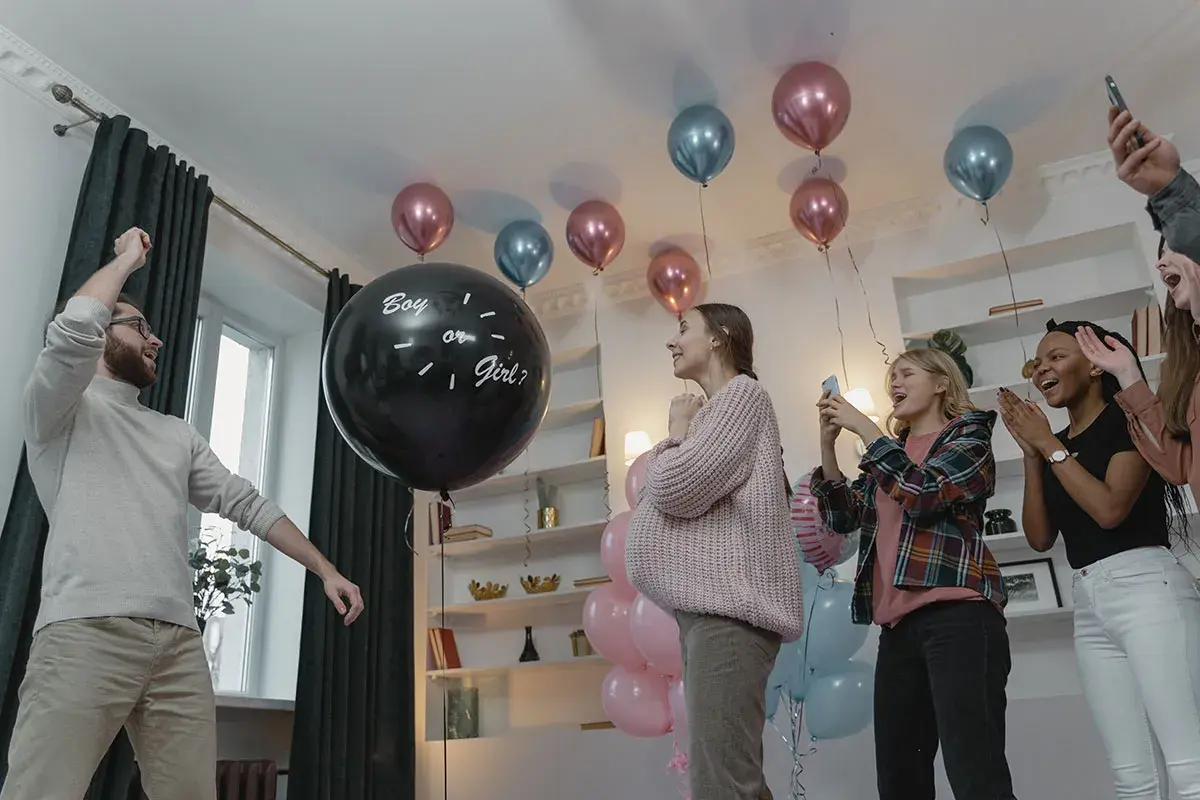 En una fiesta de revelación de género, un hombre levanta el brazo junto a un globo negro que pregunta "Boy or Girl?".
