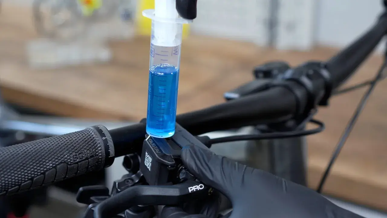 A syringe filled with blue fluid is used to bleed the brakes on a bicycle.